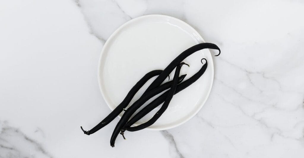 Top view of aromatic vanilla beans on a white plate placed on a marble surface, showcasing minimalist still life photography.